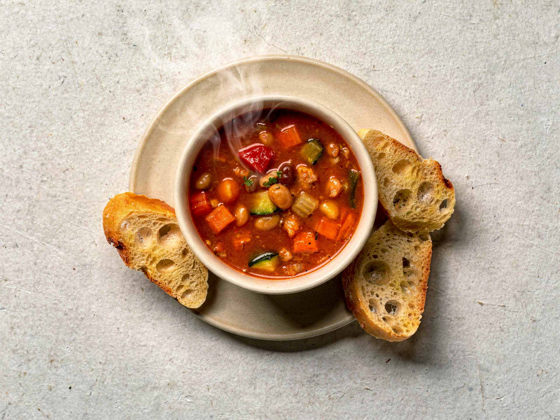Herzhafte Minestrone mit Gemüse und Bohnen in einer Schale, dampfend serviert – ideal als wärmende Mahlzeit mit frischem Brot.