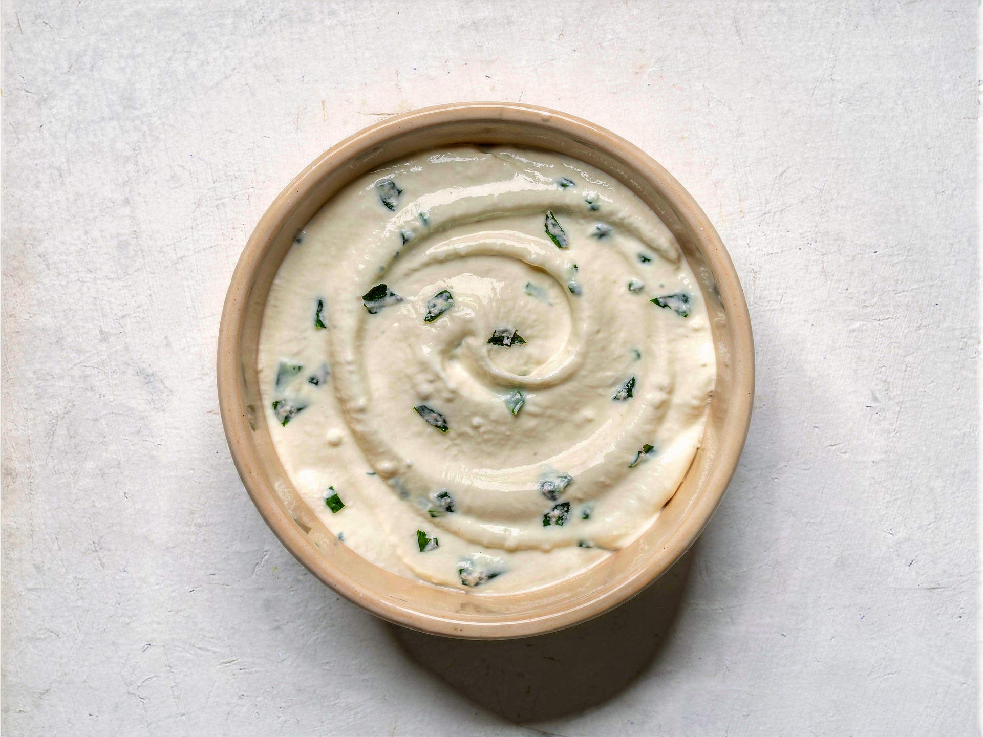 Cremiger Frischkäse-Dip mit frischen Kräutern in einer Schale, glatt gerührt mit leichter Spiralstruktur – ideal als Aufstrich oder Begleiter zu frischem Brot.
