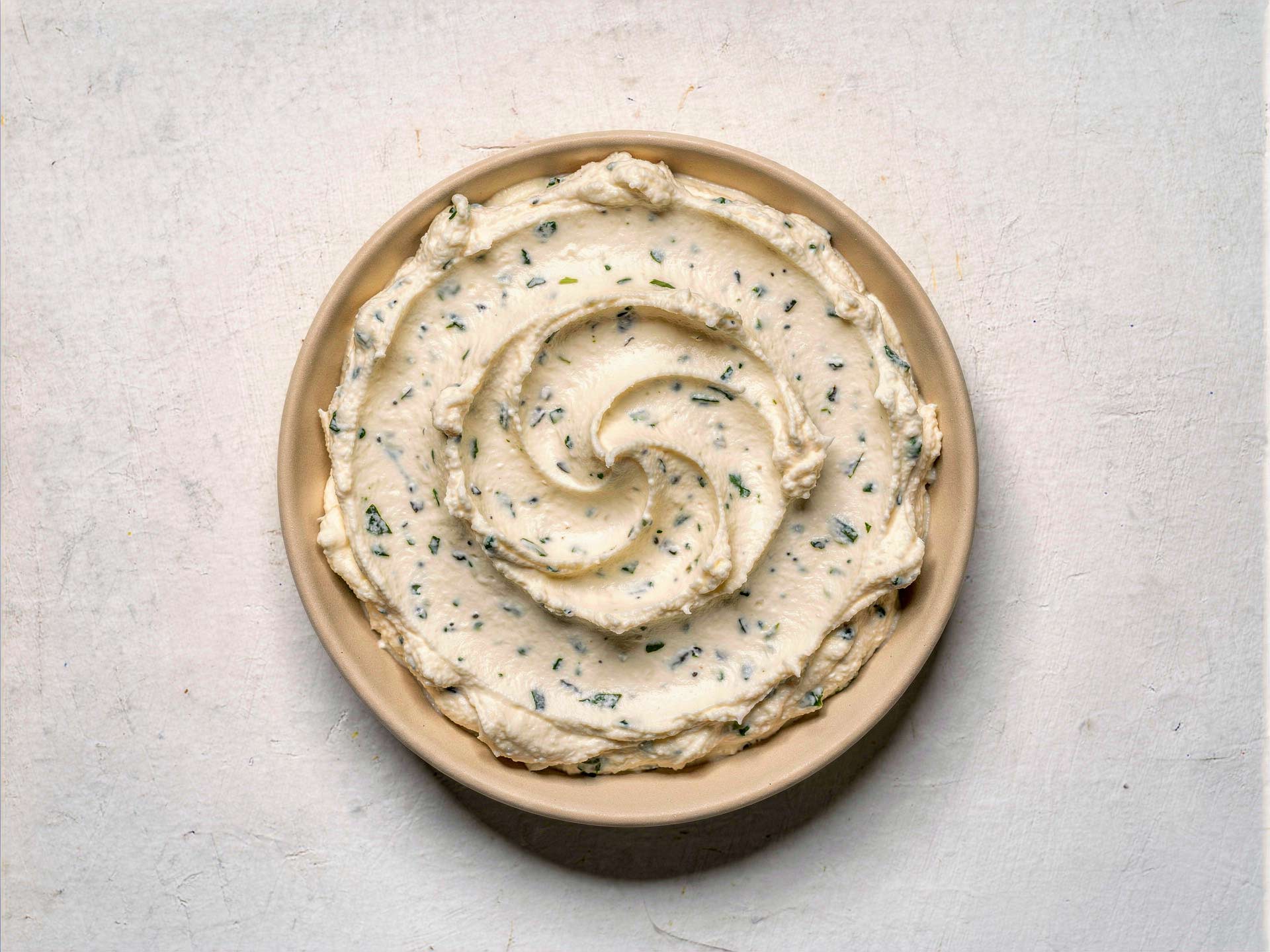 Cremiger Kräuteraufstrich in einer Schale, glatt gerührt mit feiner Spiralstruktur – ideal als Aufstrich oder Begleiter zu frischem Brot.